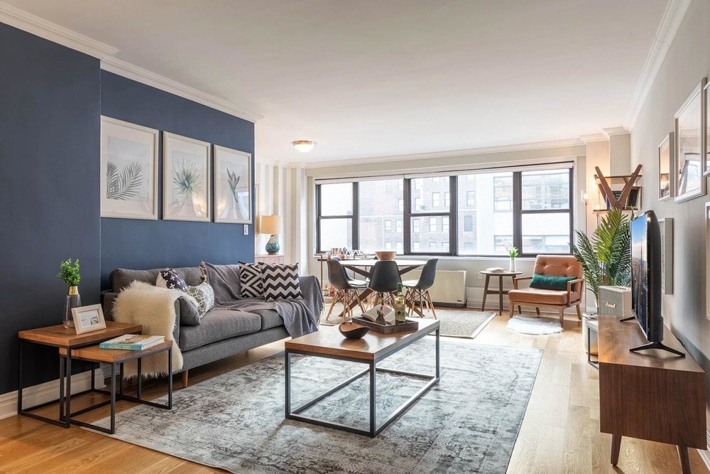 blueground Best Short Term Rental NYC kips bay living room with grey couch striped pillows wooden coffee table a grey rug and a small dining table with 3 black chairs in the back