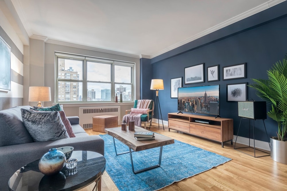blueground Best Short Term Rental NYC murray hill living room with wooden floors grey couch blue rug wooden coffee table and a big TV screen