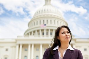 A woman with brown hair wearing a brown and white shirt is standing in front of the U.S. Capitol building in Washington, D.C.