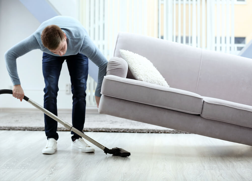 a man vacuuming underneath his couch