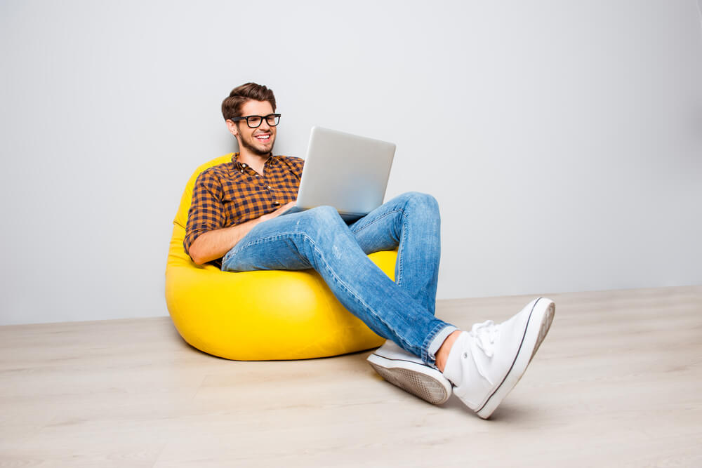 man working on his laptop freelancing and laying comfortably on a yellow beanbag chair