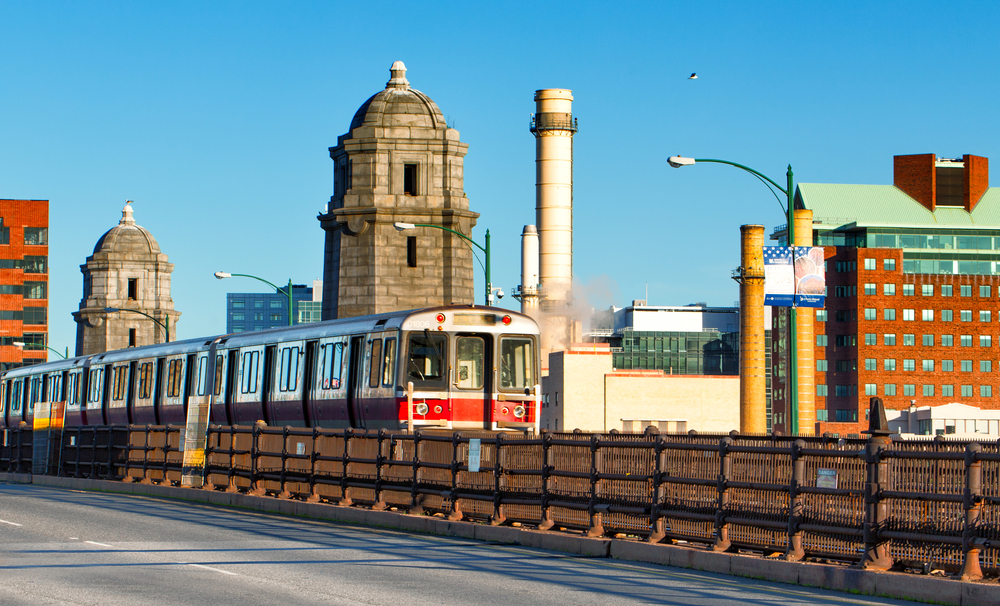 a commuter train in Boston passes over a bridge with a view of city buildings in the background