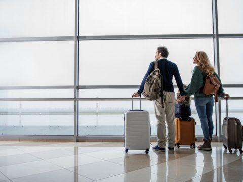 couple standing at the airport with their suitcases looking out the window in the middle of moving abroad