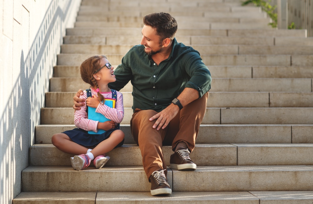 father and daughter sitting on the steps of the school and smiling