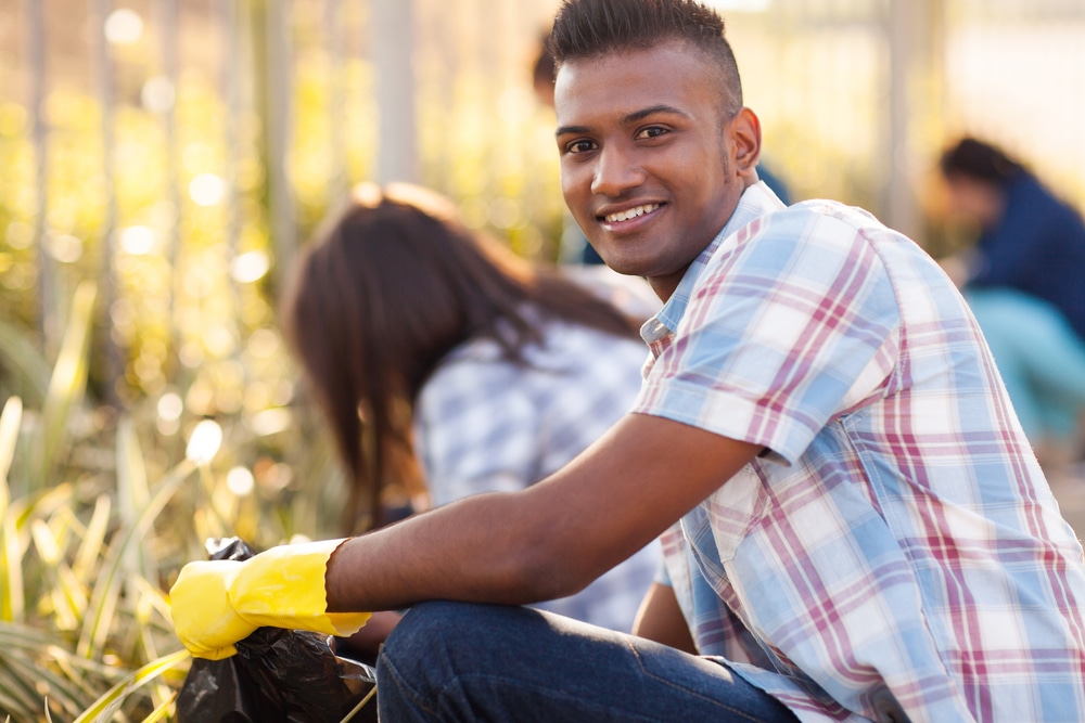 young man with a blue and red plaid shirt and yellow plastic gloves is smiling while cleaning