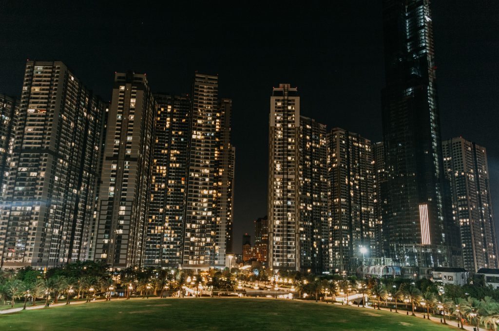 some high rise apartment buildings lit up at night next to a green grassy area