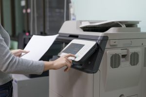 a person wearing a gray sweater is using a copy machine and holding a piece of paper in their left hand
