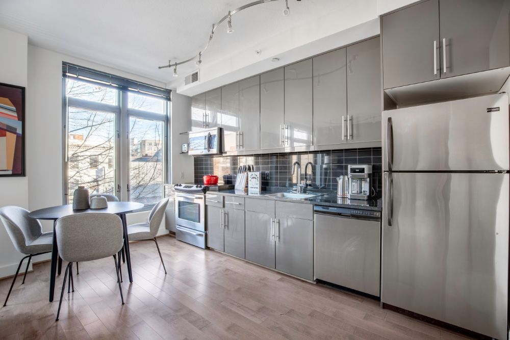 A fully furnished apartment in Washington, D.C. managed and designed by Blueground. The kitchen has stainless steel appliances and a small circular table with four chairs next to a large window