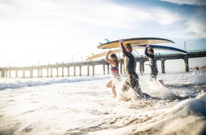 three surfers walk into the water near the pier in Los Angeles