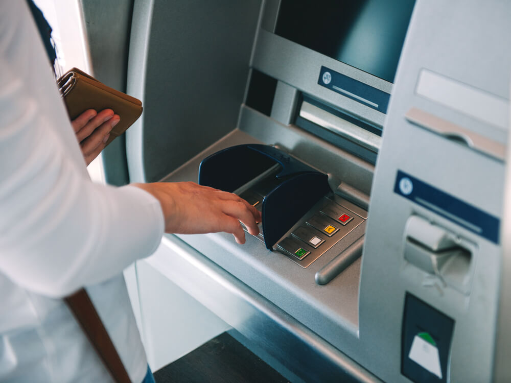 someone wearing a white shirt holding a brown wallet in one hand and pressing buttons on an ATM machine with the other hand
