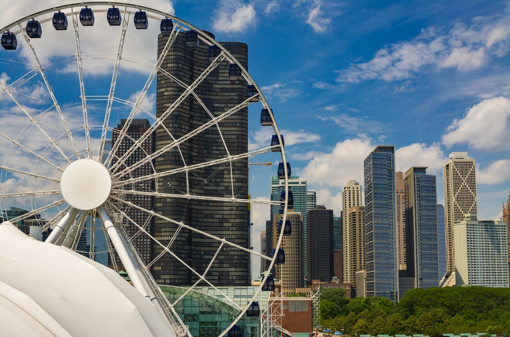 A view of tall, modern buildings and high rises through a large white ferris wheel 