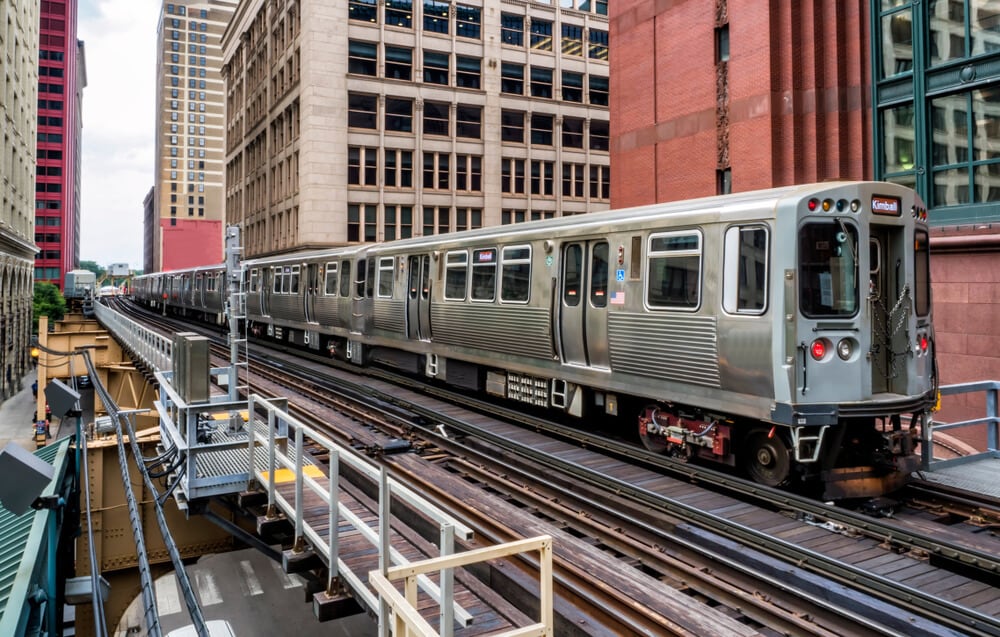 a large metal subway train on the tracks in Chicago stopped between many tall buildings 