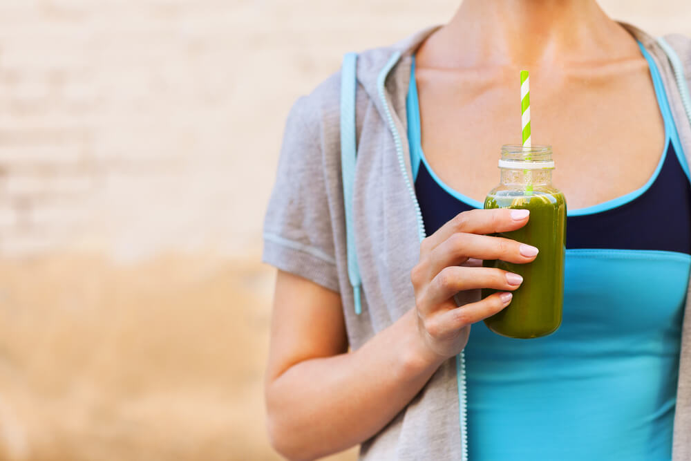 woman wearing exercise clothes drinks a green juice after the gym