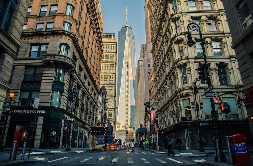 A New York City street with classical buildings on either side and the One World Trade Center straight ahead