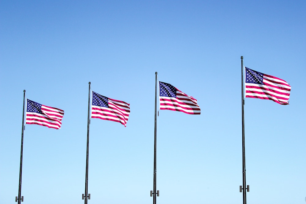 Four American flags on posts waving in front of a clear blue sky