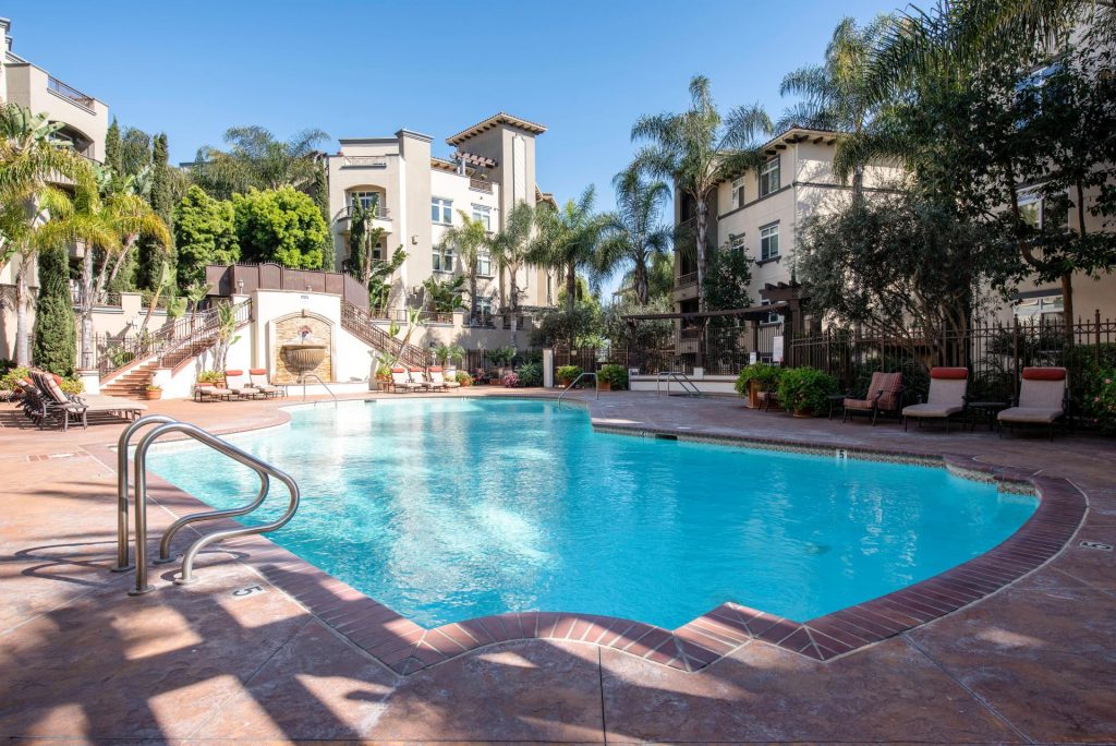 an outdoor pool area at a los angeles apartment building. there are some lounge chairs on the right side and the pool ladder on the lefft