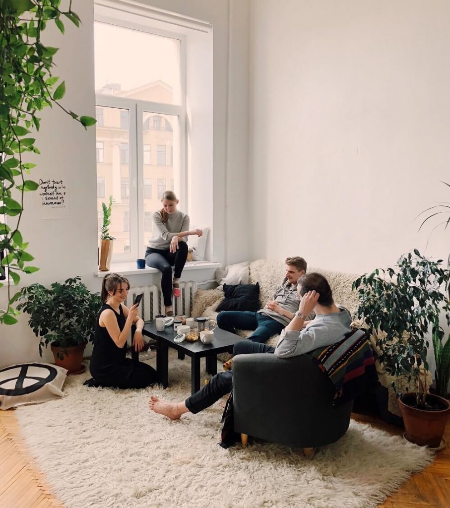 a group of friends sitting around in a modern living room talking to each other