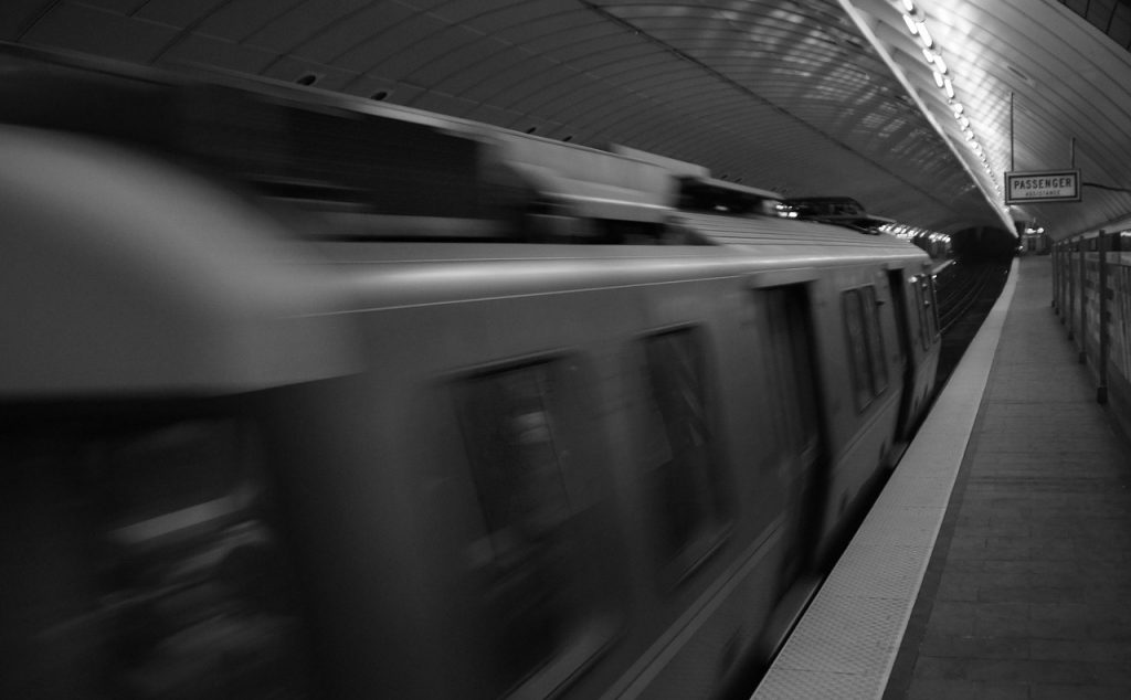 A black and white photo of a subway train moving forward as it approaches the subway platform