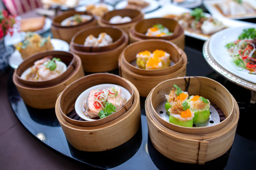 a large round table full of dim sum bowls and other plates of Asian food