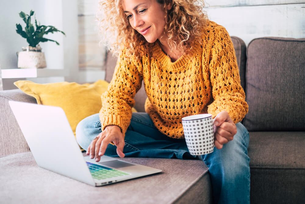 woman in a yellow sweater holding a coffee mug and working on the computer as a freelancer