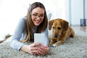 Girl lying on rug with her dog looking at smartphone