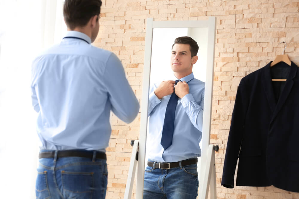 man looking in a mirror adjusting his tie and deciding how much he is worth 