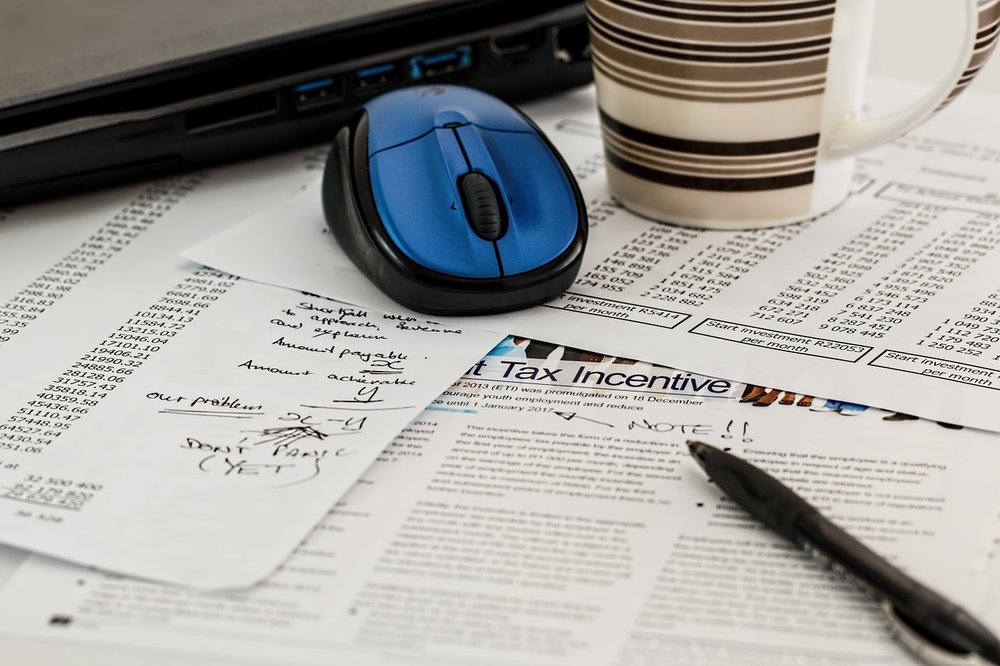 table with many tax papers, a pc and a coffee mug