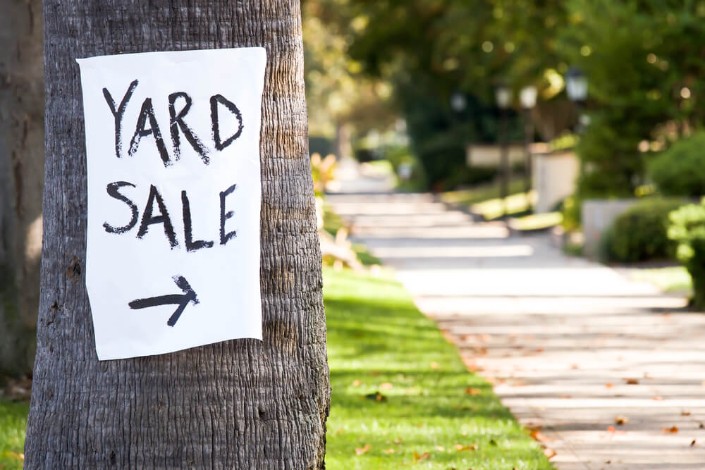 white poster with black text spelling 'yard sale' pinned to a tree on a grassy street