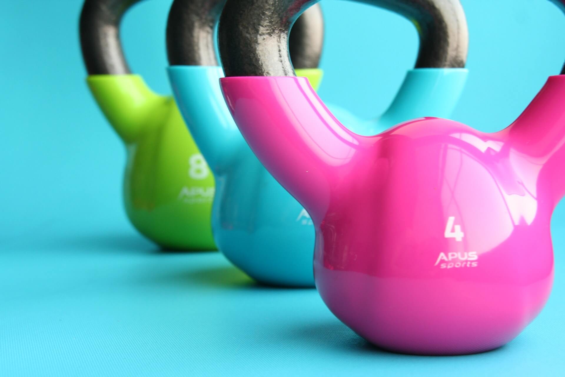 three brightly colored kettle bells on a bright blue surface