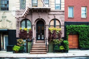 The beautiful and detailed doorway of an New York City apartment building. There is a small staircase outside of the door as well as bushes and greenery