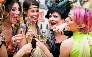 a group of girlfriends at a festival, dressed up in costumes and drinking champagne