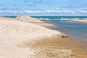 sand dunes and shoreline with blue sky and whispy white clouds in the backgrounds