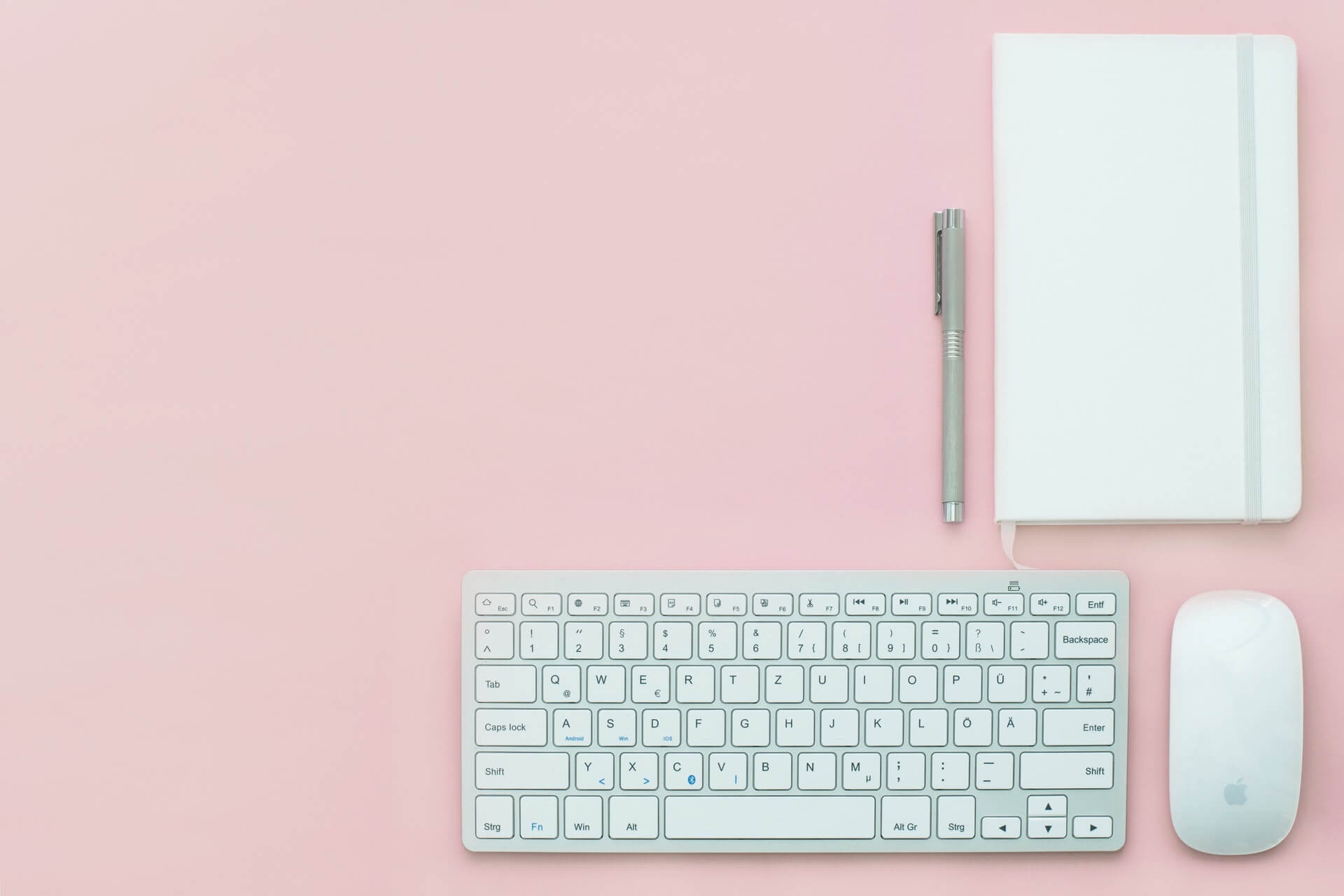 home office ideas white desktop keyboard notebook and pen on a pink background 