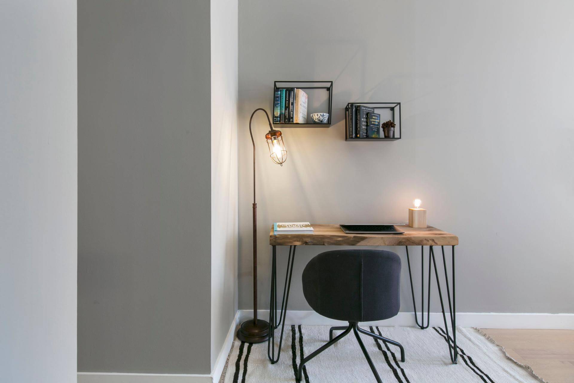 home office ideas Blueground desk space in an NYC apartment. There is a wooden table with a laptop, a book and a lamp on it and a black chair in front of the chair. Next there is a floor lamp and underneath there is a white rug with black stripes.