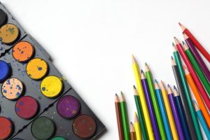 a paint set and colored pencil set laying on top of a white table
