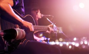 a close up shot of a man playing a black electric guitar which is held in front of a microphone next to a woman singing