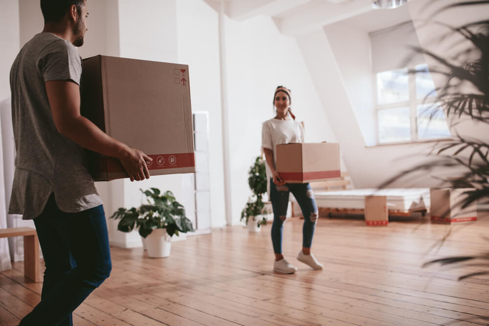 A young couple holding cardboard boxes is walking through their new apartment
