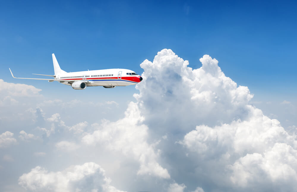 A large white plane with a red and blue design is flying through large white clouds with a clear blue sky in the background