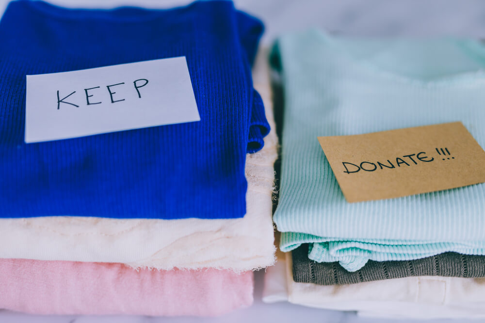 piles of shirts and sweaters in various colors split into two separate piles in order to decide what is for keeping and what is for donating