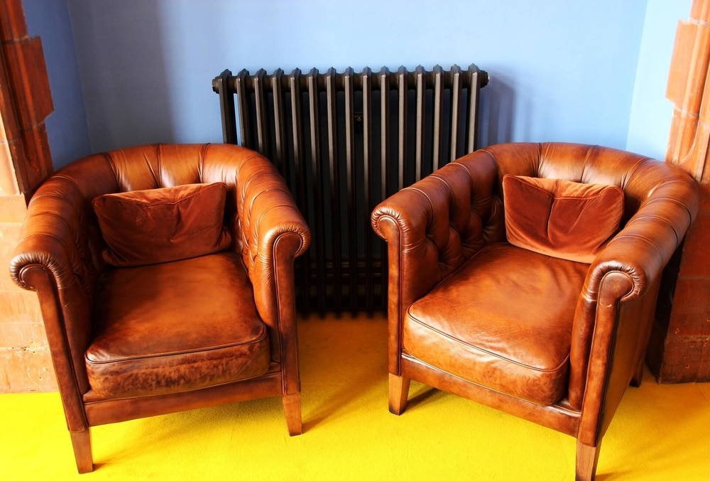two brown leather chairs in front of a heater 