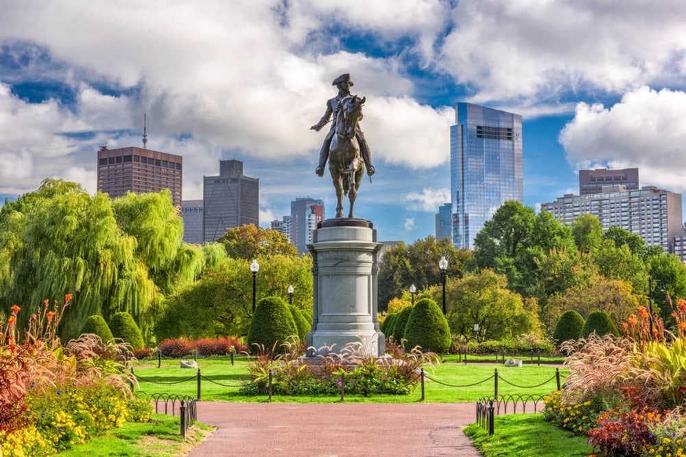 statue in park in Boston of a man sitting on horse with city scape in the background and trees all around