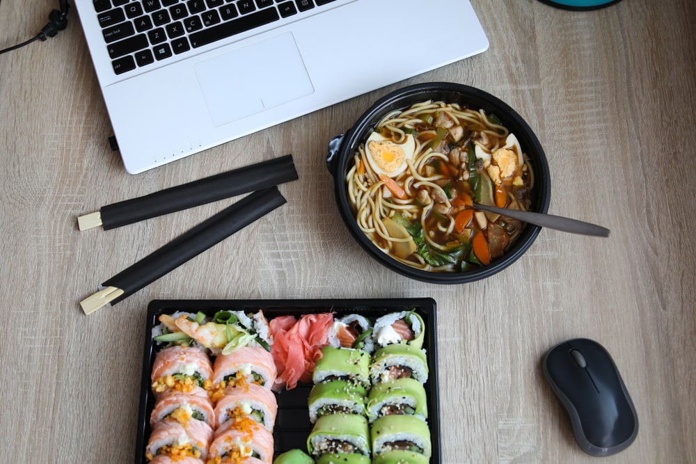 Take away ramen soup and sushi plate next to a laptop 
