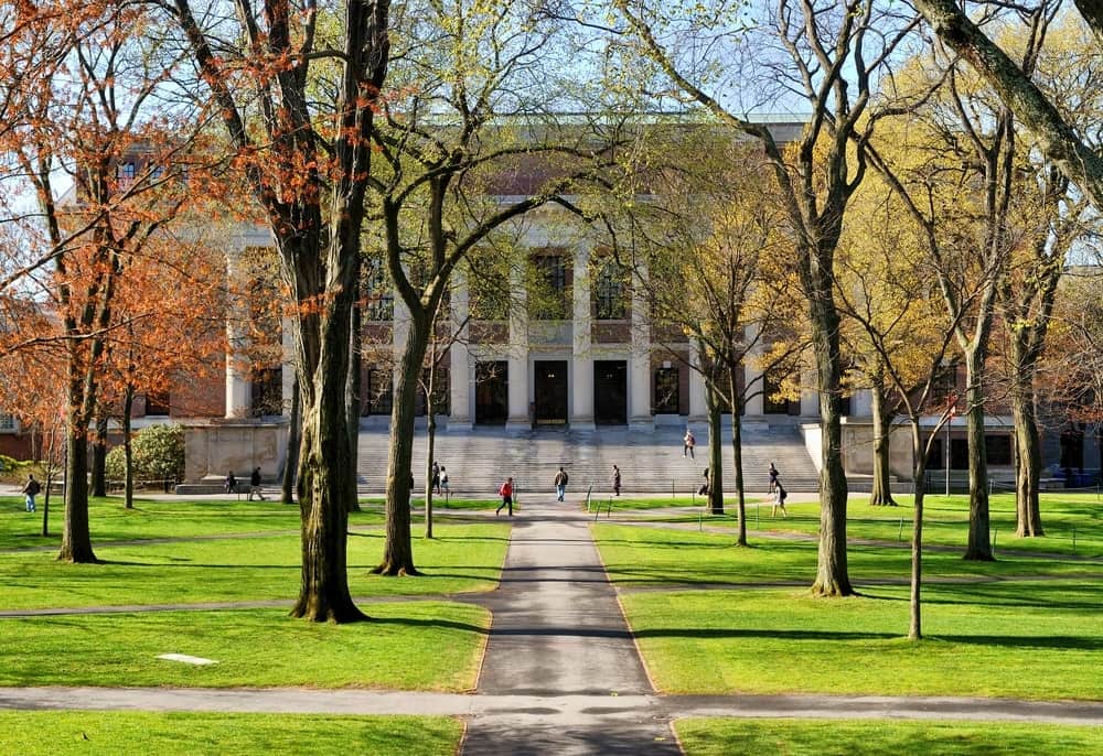 A large building with tall white columns sits on the Harvard Campus surrounded by fall foliage and bright green grass