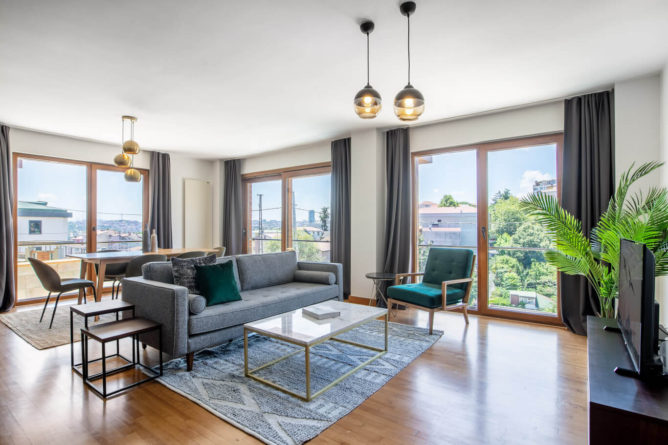 A furnished and equipped apartment in Istanbul, Turkey managed by Blueground. There is a grey couch and a white marble coffee table over a grey rug. There are many windows on each wall and hanging light fixtures on the ceiling