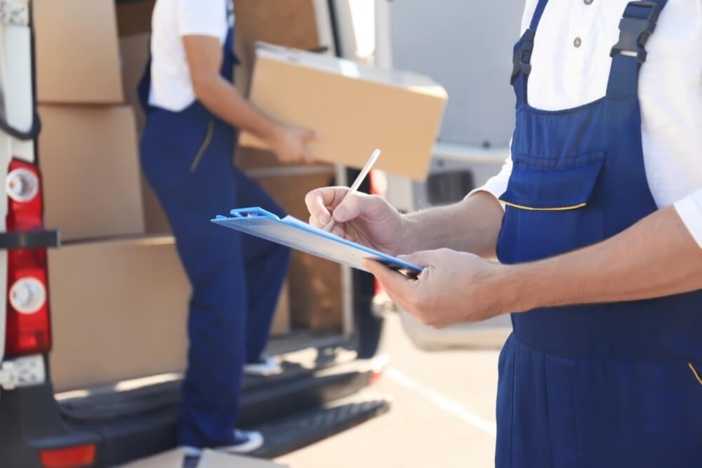 movers wearing blue overalls holding clipboard and holding a box