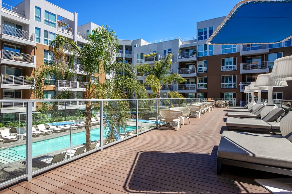 The large outdoor pool complex of an apartment building in west hollywood los angeles california. There are many trees as well as large comfortable chairs.