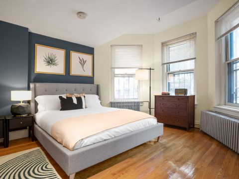 blueprint blueground studio apartment Boston bed next to heater and grey headboard against dark green paint