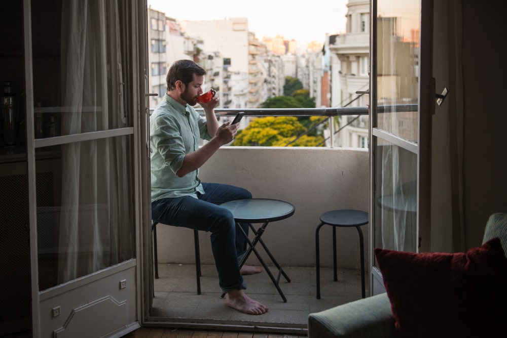 man with beard reading phone and drinking coffee on terrace