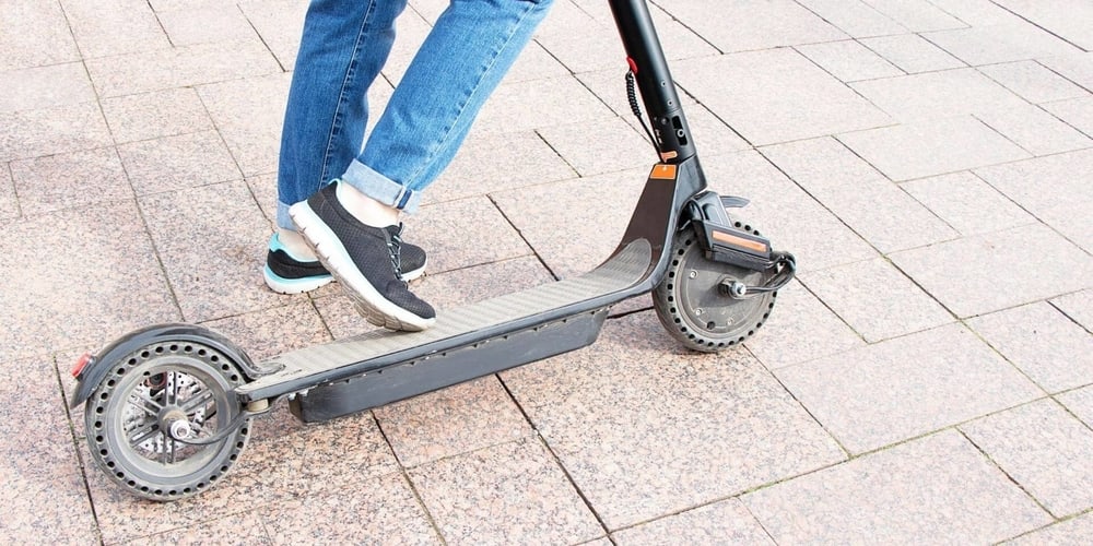 a person wearing black shoes and blue jeans is stepping on to his black bird scooter