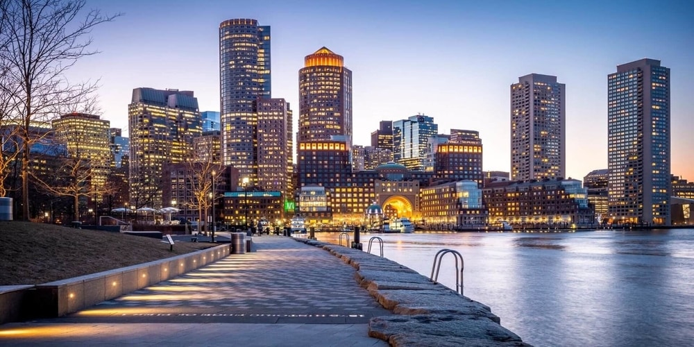 boston city skyline at night with all the buildings lit up and a body of water in the right half of the image